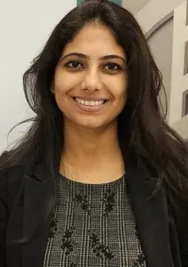 A woman with long dark hair smiling, wearing a dark blazer.